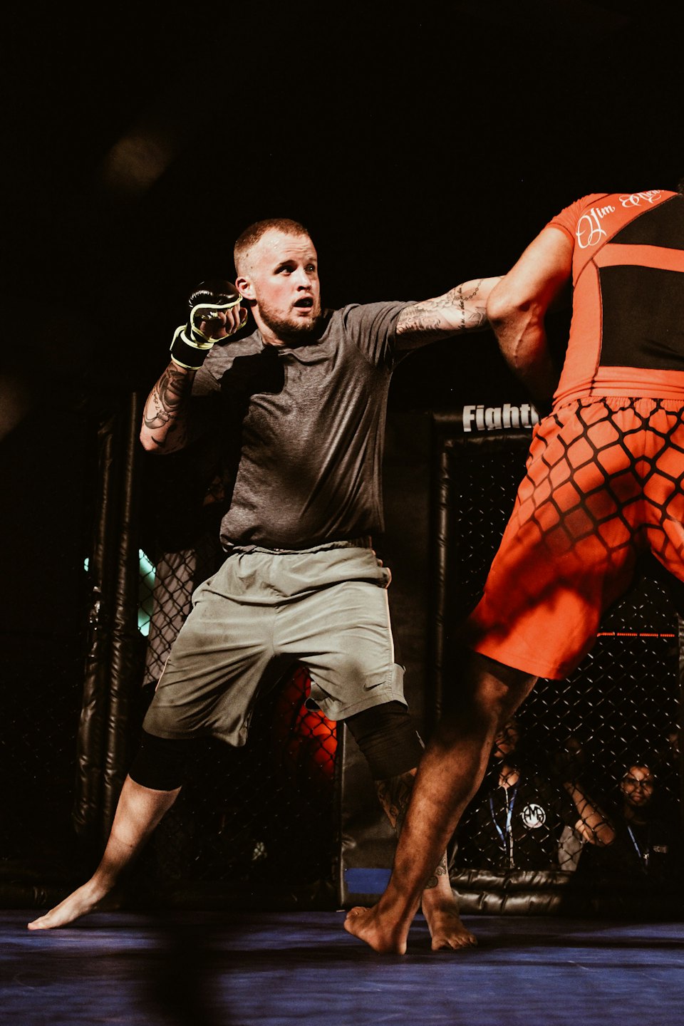 Two mixed martial arts fighters spar inside a chain-link cage.