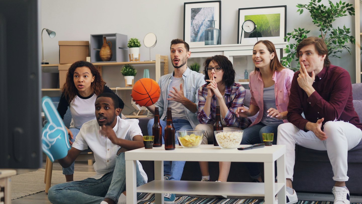 Six friends watch a sports game together in a living room.