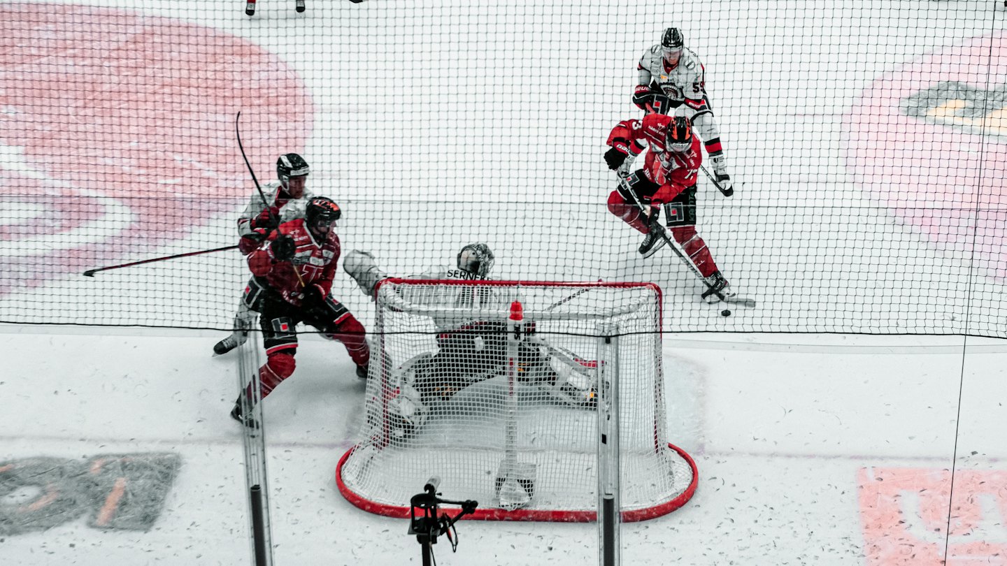 Ice hockey players battle for the puck near the net on a bright rink.
