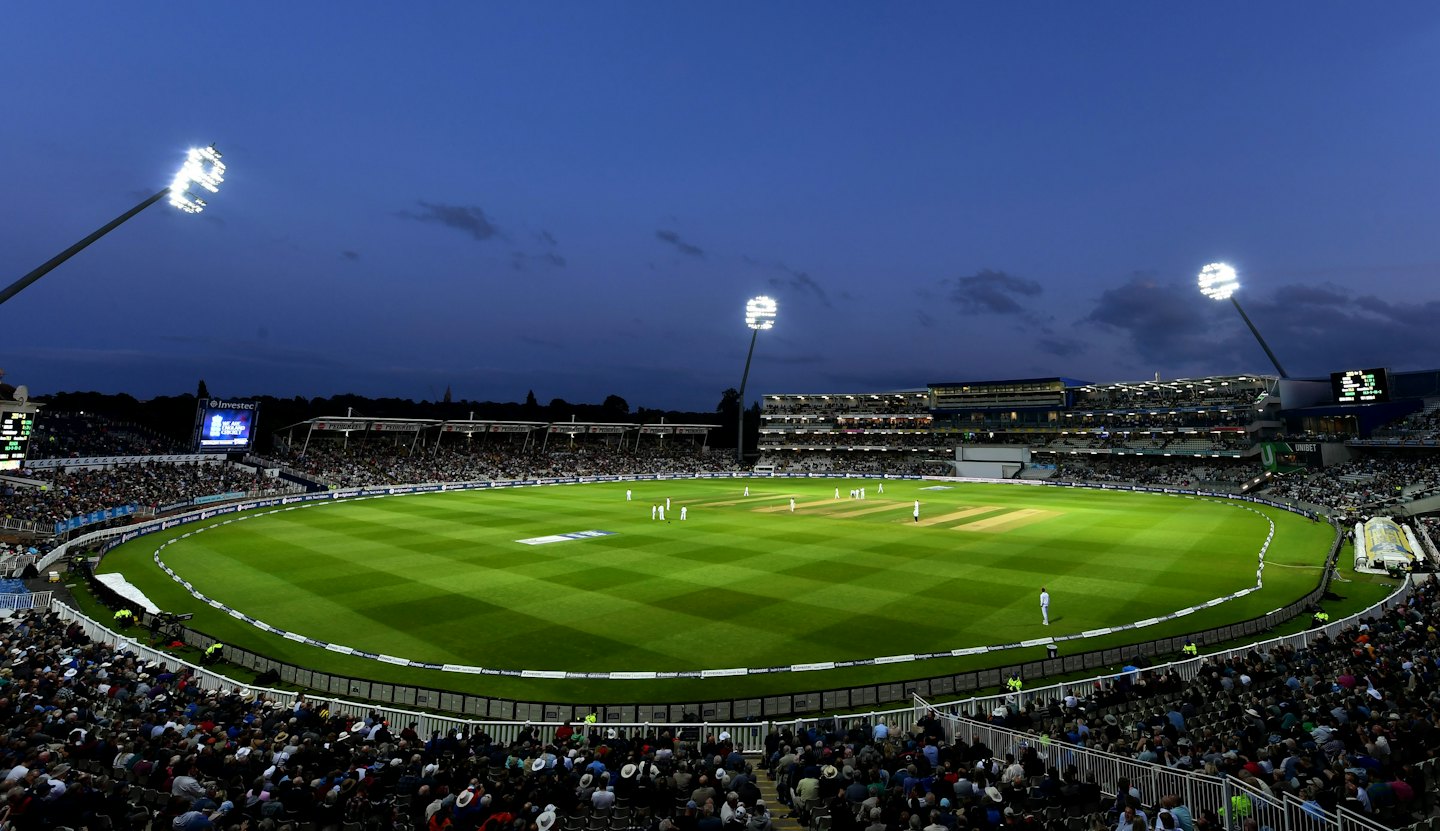 Cricket match played under floodlights at dusk stadium.